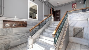 A marble staircase with a wooden handrail, a wall-mounted mirror, and a door with a poster.