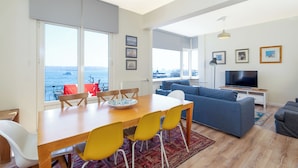 A modern living room with a dining area, large windows, and a television.