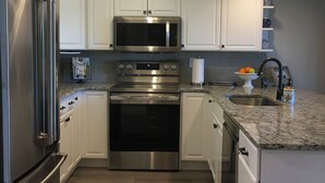 A modern kitchen with stainless steel appliances, white cabinetry, and a granite countertop.