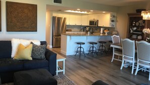A modern kitchen with stainless steel appliances, a central island with bar stools, and a dining area with white chairs.