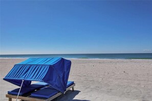 Ein Strandstuhl mit blauem Sonnendach am sandigen Strand.
