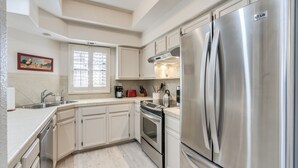 A modern kitchen with white cabinets, stainless steel appliances, and a large refrigerator.