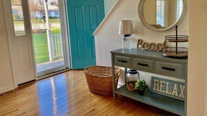 Une pièce avec un plancher en bois, une porte de couleur turquoise, un miroir, une lampe, un panier et une pancarte indiquant « Détendez-vous ».