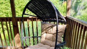 Une chaise en osier avec un coussin, une petite table en bois et une plante en pot sur une terrasse en bois.