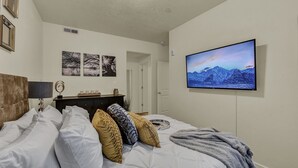 Ein Schlafzimmer mit einem Bett, einem an der Wand montierten Fernseher und gerahmten Bildern.