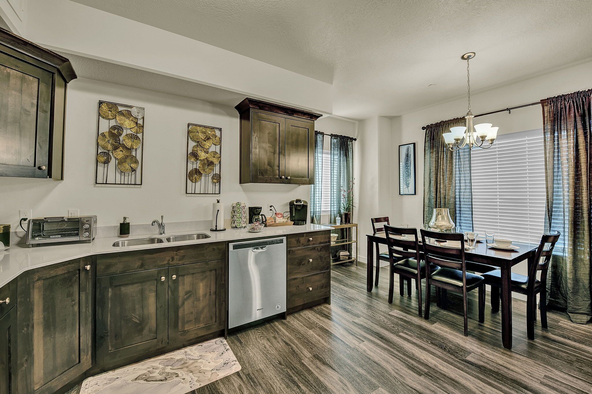 A modern kitchen with dark wood cabinets, a dishwasher, and a dining area with a chandelier.