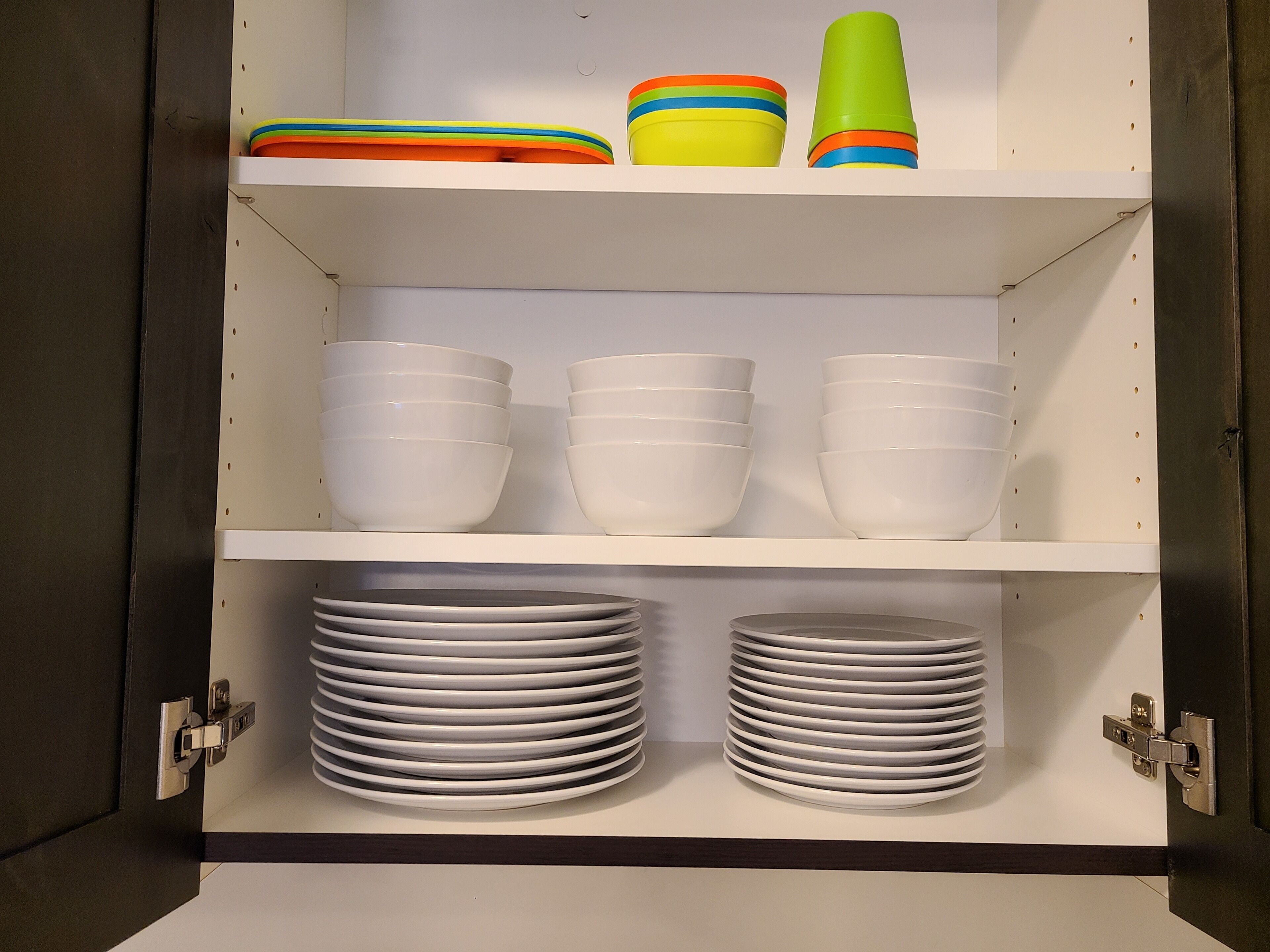 Un mueble con estantes blancos que contiene cuencos blancos, platos y recipientes de colores.