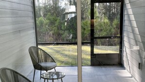 Ein modernes Interieur mit Glastür zu einem Balkon. Zwei Korbstühle und ein kleiner Tisch sind vorhanden. Der Raum hat Holzböden und ein Fischgrätmuster an den Wänden.