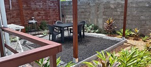 Ein Terrassenbereich mit Tisch und Stühlen, umgeben von Pflanzen und einem Holzzaun.