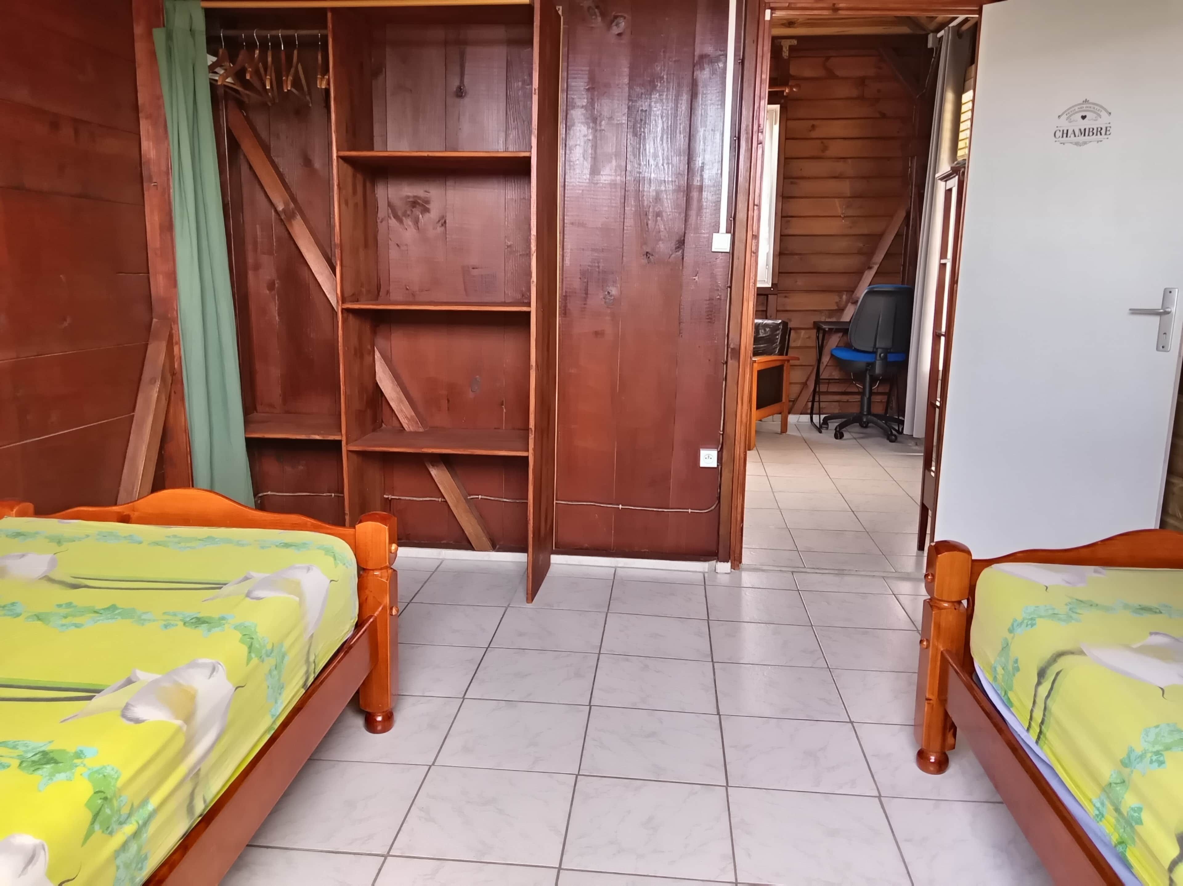 A room with two wooden beds, a wooden wardrobe, a desk, and a chair.