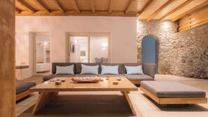 A modern living room with a wooden ceiling, stone wall, and a sofa set with patterned cushions.
