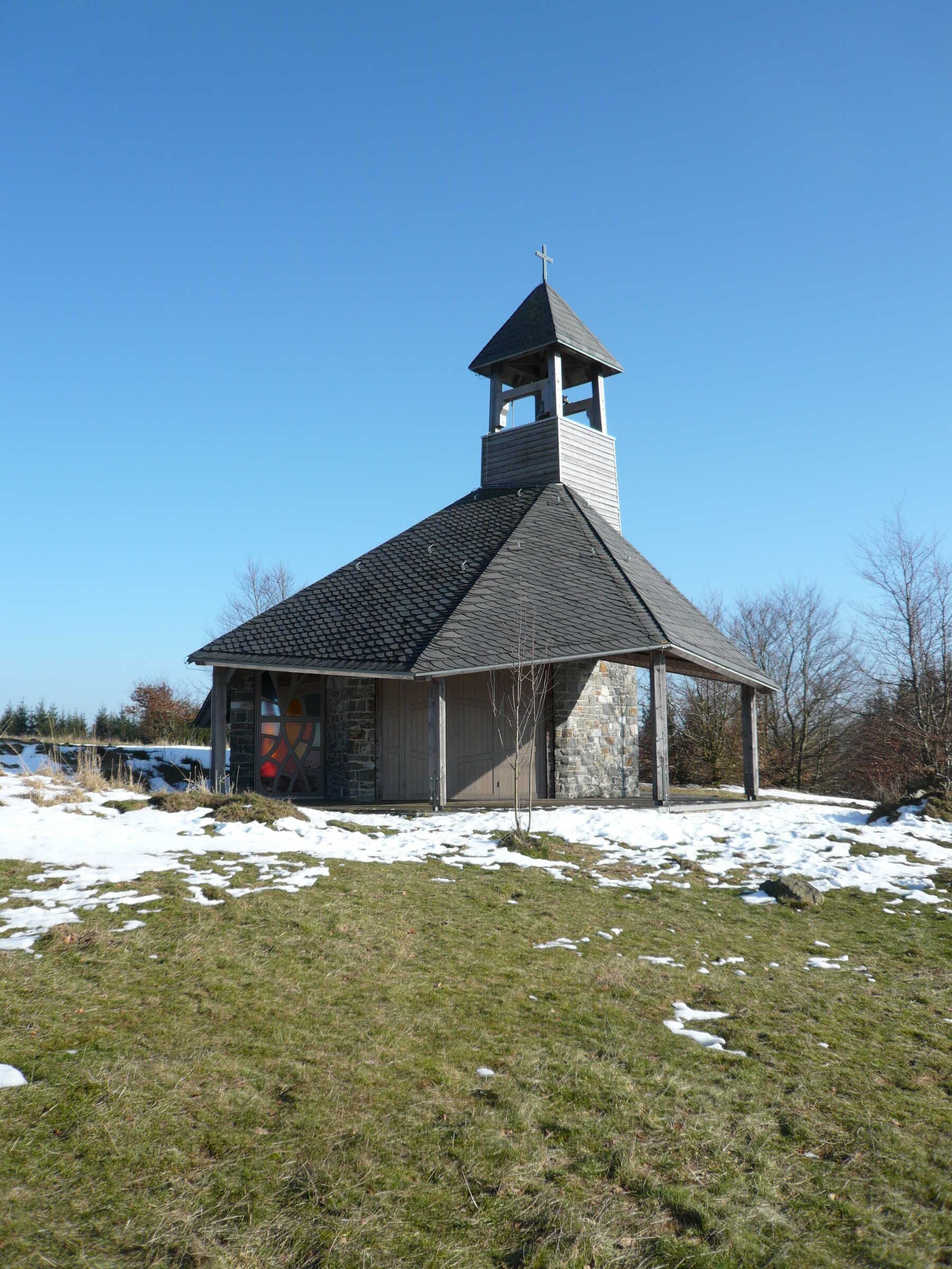 Une petite église dotée d’un clocher et d’un campanile, entourée d’un paysage enneigé.