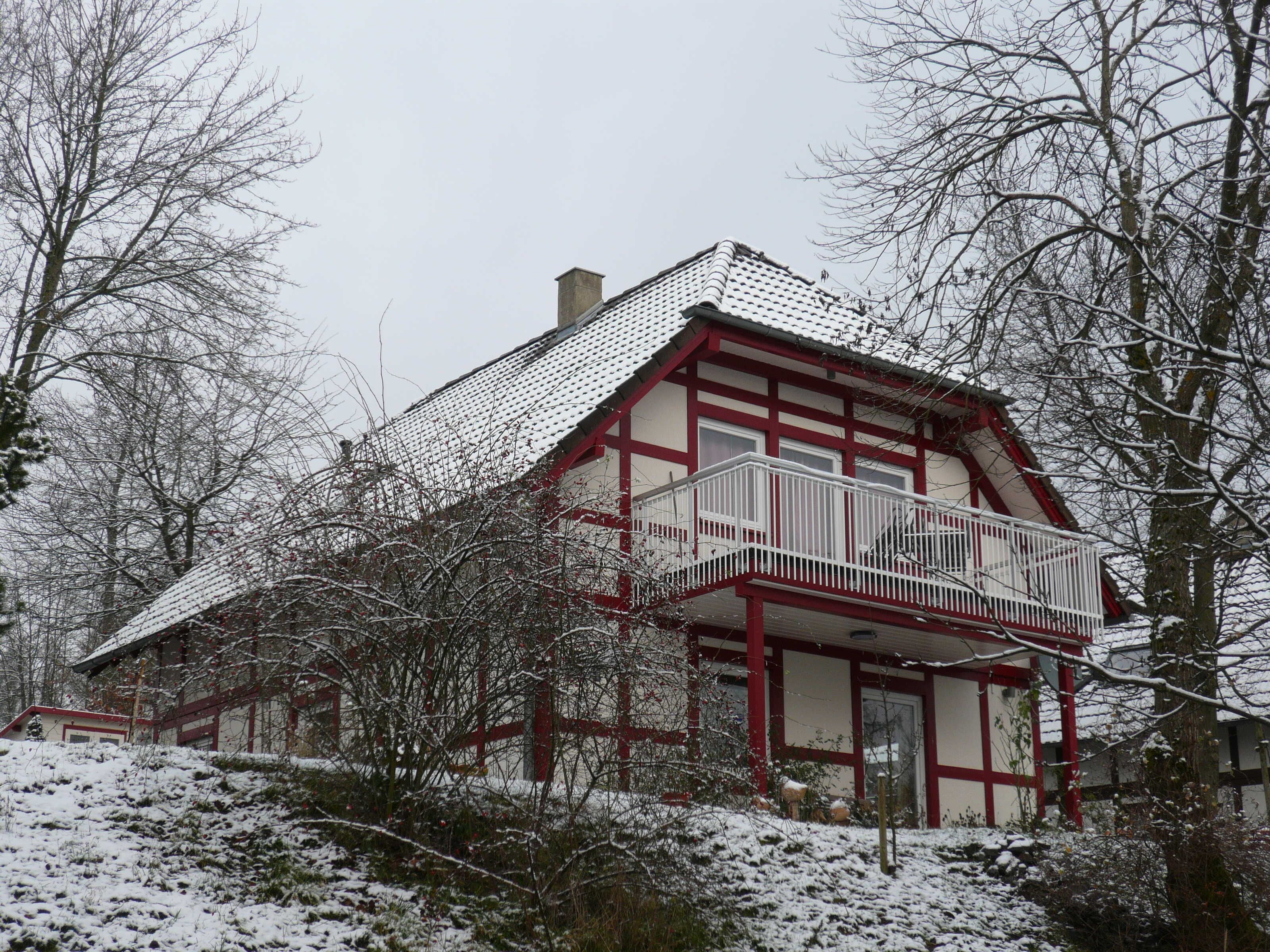 Ein zweistöckiges Haus mit Balkon, umgeben von schneebedeckten Bäumen.