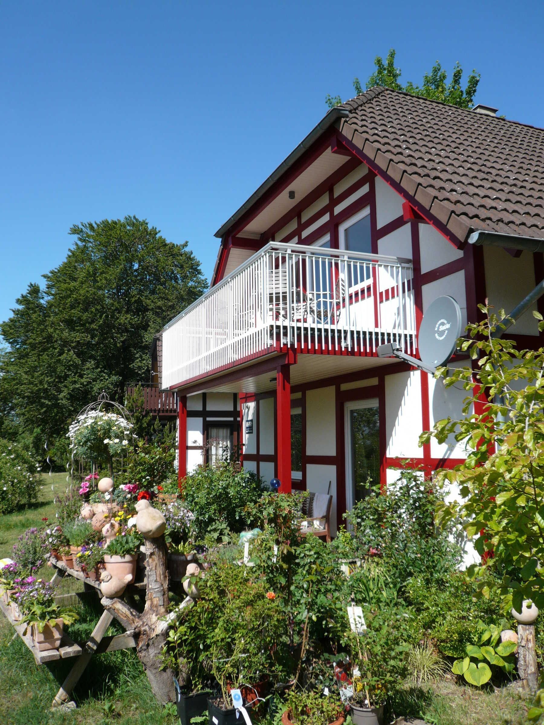 A two-story building with a balcony, surrounded by a garden with various plants and flowers.
