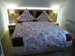 A neatly made bed with floral bedding, a bedside table, and a wall-mounted lamp. - Die Wohlfühloase, Deutschland (Frankenau)