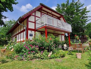 A traditional building with a balcony, surrounded by a well-maintained garden with various flowers and plants. - Die Wohlfühloase, Deutschland (Frankenau)