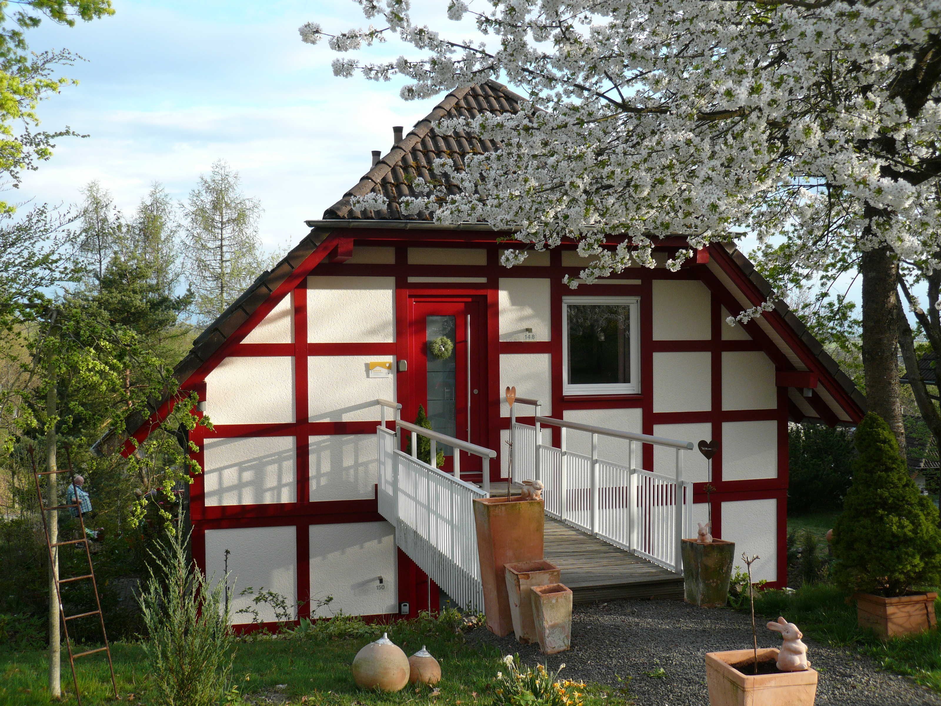 A traditional half-timbered house with a red door, white walls, and a wooden staircase leading to a porch.