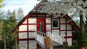A traditional half-timbered house with a red door, white walls, and a wooden staircase leading to a porch.