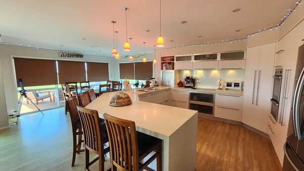 A modern kitchen with a central island, wooden chairs, and pendant lighting. - Tranquil & private house, outdoor pool, rural setting close to beaches & hikes (Whangarei)