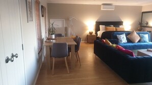 A modern living room with a blue sofa, a wooden dining table, and a hanging plant. - Tranquil & private house, outdoor pool, rural setting close to beaches & hikes (Whangarei)