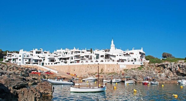 A coastal town with white buildings, rocky shoreline, and boats in the water.