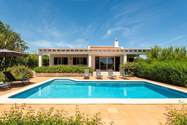 Una casa moderna con piscina, terraza cubierta y jardín.