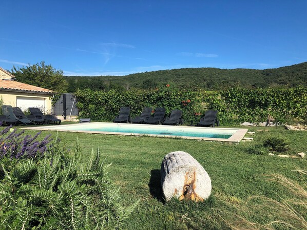 A swimming pool with lounge chairs, a stone in the foreground, and a house in the background.