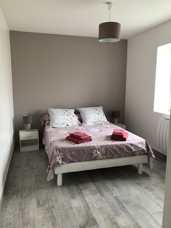 A bedroom with a bed, two nightstands, a hanging lamp, and a window.