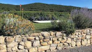 Un muro de piedra, una piscina con sillones de descanso y un paisaje montañoso de fondo.