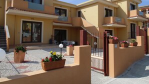 Un edificio residenziale a più piani con balconi, ingresso carrabile e area salotto all'aperto.