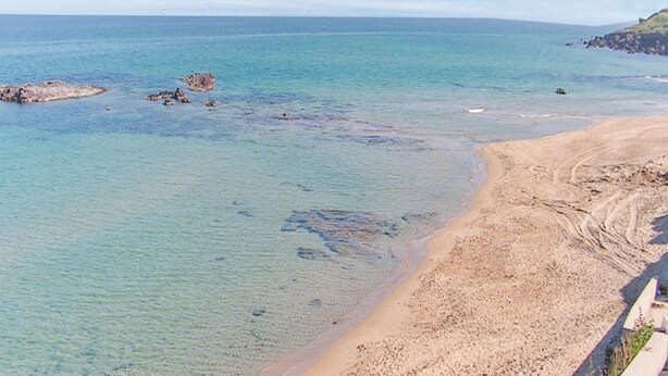 Una spiaggia con acque cristalline turchesi, una riva sabbiosa e affioramenti rocciosi.