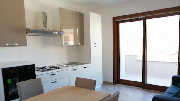 A modern kitchen with white cabinets, a gas stove, and a dining area with a wooden table and chairs. - Apartment Sleeps 4 With Free Parking (Badesi)