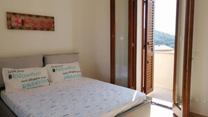 A bedroom with a bed, two pillows with motivational text, a wooden door, and a view of the outdoors. - Apartment Sleeps 4 With Free Parking (Badesi)