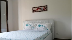 A bedroom with a white bed, a white headboard, and a wall-mounted painting. - Apartment Sleeps 4 With Free Parking (Badesi)
