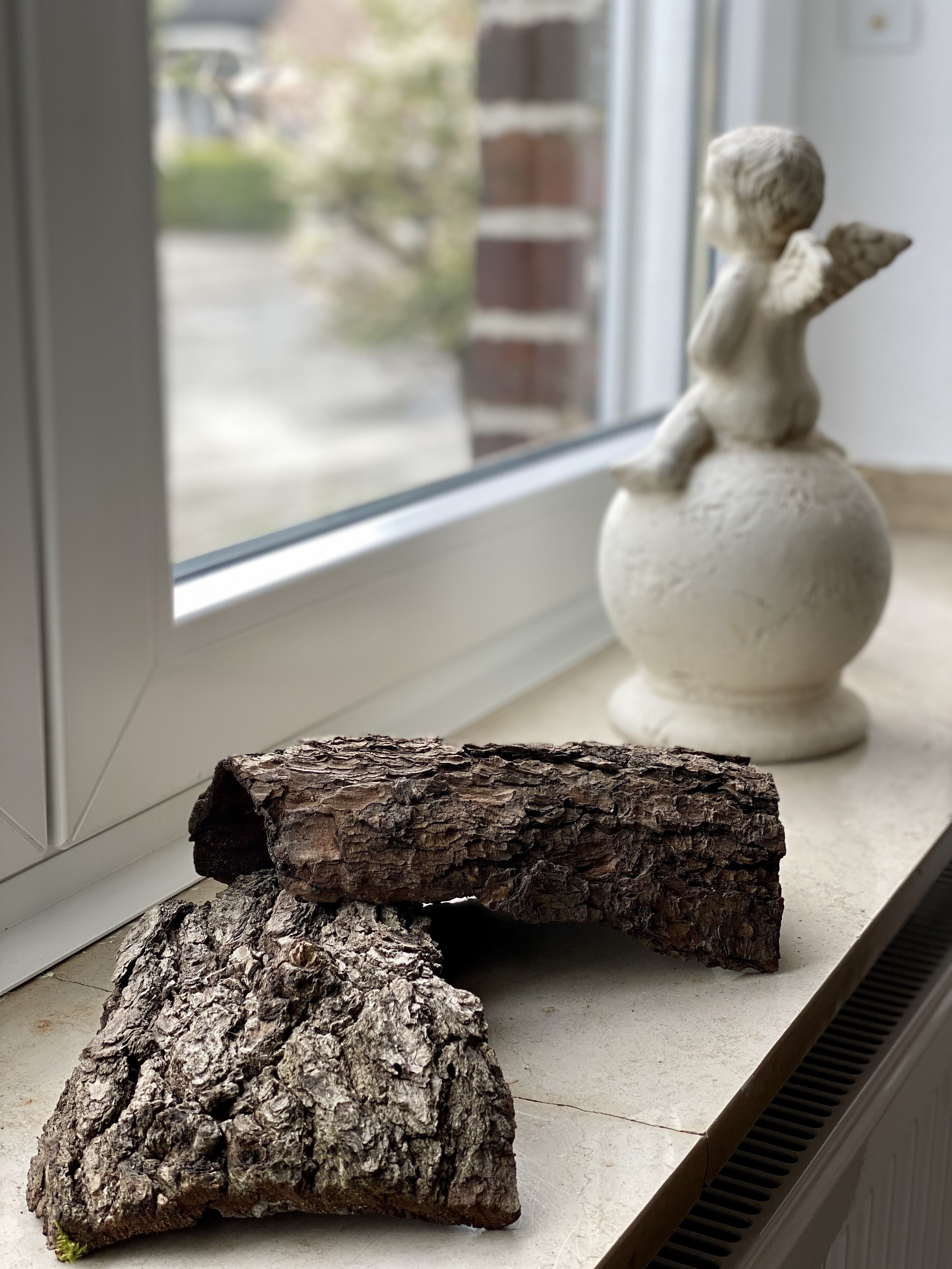 Un rebord de fenêtre orné d’une bûche de bois et d’une statue blanche.