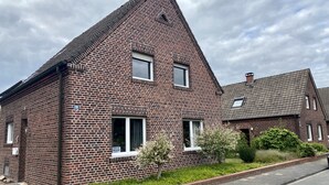 Ein Backsteinhaus mit Satteldach, kleinem Garten und gepflasterter Auffahrt.