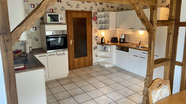 Eine kleine Küche mit weißen Schränken, einer Mikrowelle, einem Backofen und einer Kaffeemaschine.