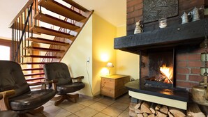 Ein gemütliches Wohnzimmer mit Kamin, Holzstühlen, einem kleinen Tisch und einer Treppe.