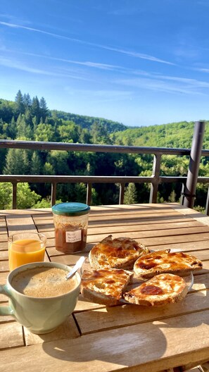 A wooden table with a glass of orange juice, a jar of peanut butter, a bowl of oatmeal, and several slices of toast with jam.