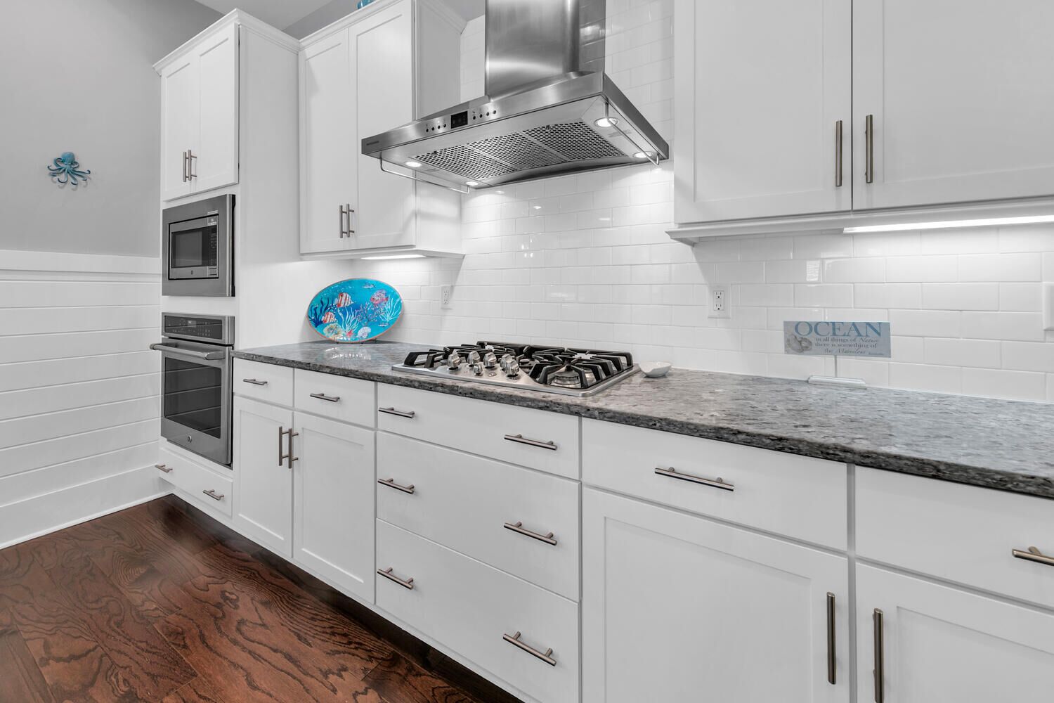 A modern kitchen with white cabinetry, a stainless steel range hood, a gas stove, and an oven.