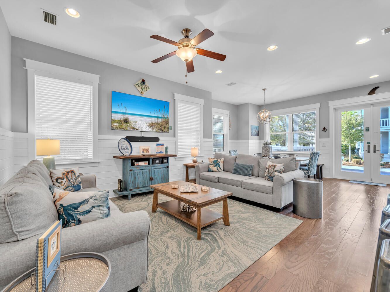 A spacious living room with a ceiling fan, large windows, and a view of the outdoors.