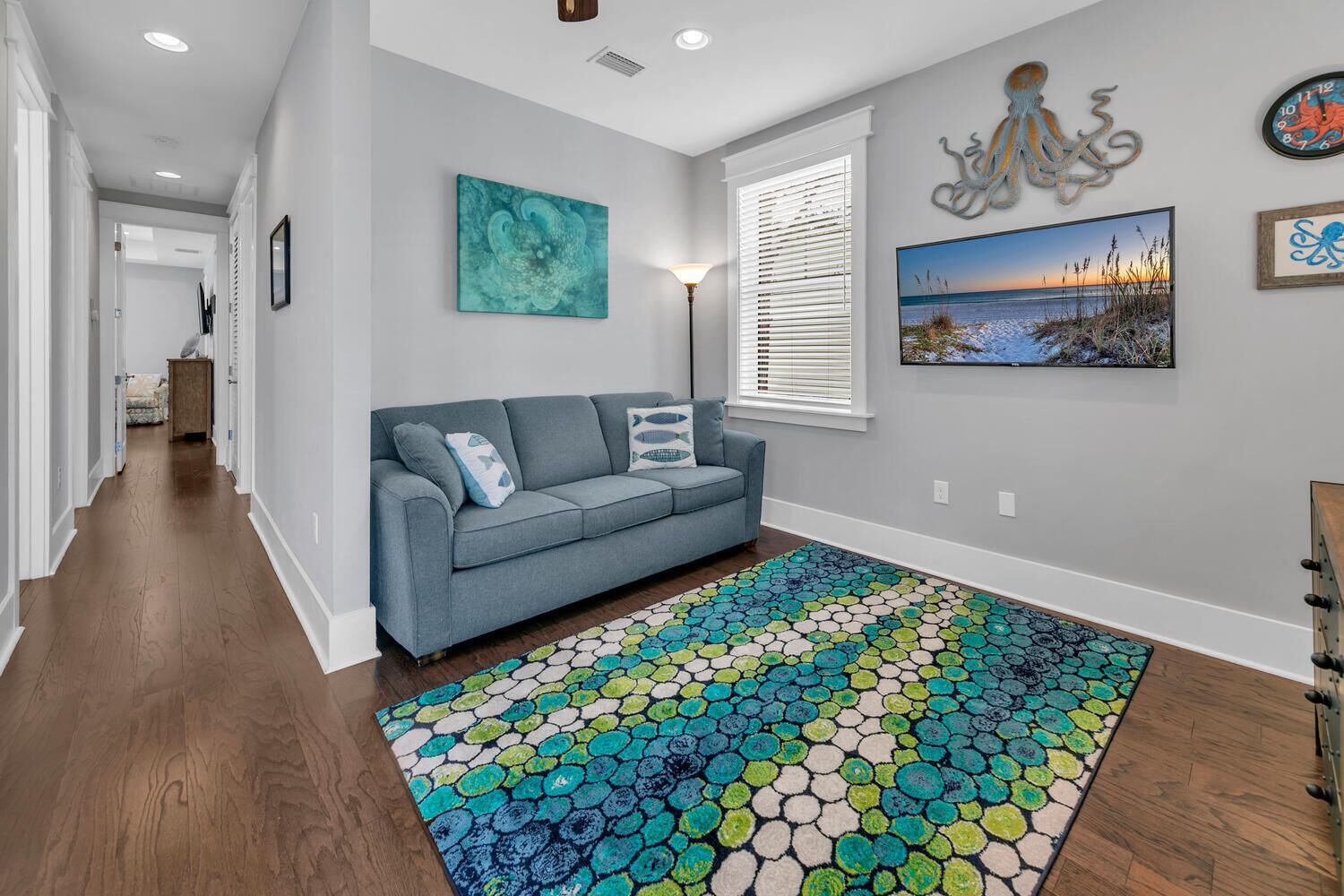 A hallway with a grey sofa, a colorful rug, and wall art including an octopus and a seascape.
