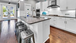 A modern kitchen with white cabinets, a granite countertop, stainless steel appliances, and a large island with bar stools. - 🐙Golf Cart + Bikes Included-Pools-2 Masters-Octopus's Garden🐙 (Santa Rosa Beach)