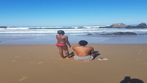 Dos personas en una playa arenosa, con olas al fondo.