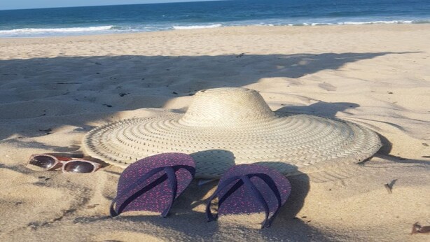 Una playa con un sombrero de paja y chanclas sobre la arena.