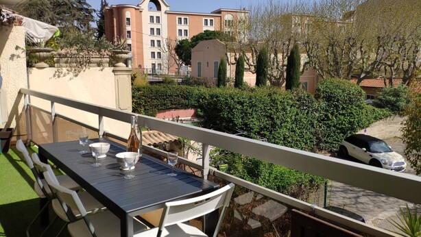 A balcony with a table set for two, overlooking a residential area with a row of houses and a parked car. - Modern 4-star 2-bedroom apartment in the center of Aix with parking and terrace (Aix-en-Provence)