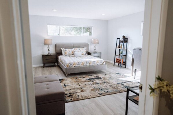 Un dormitorio con cama, mesitas de noche, una alfombra, una silla y un escritorio.