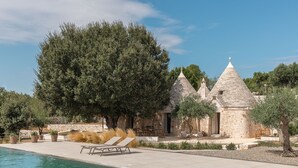 A stone building with a pool, lounge chairs, and a large tree.