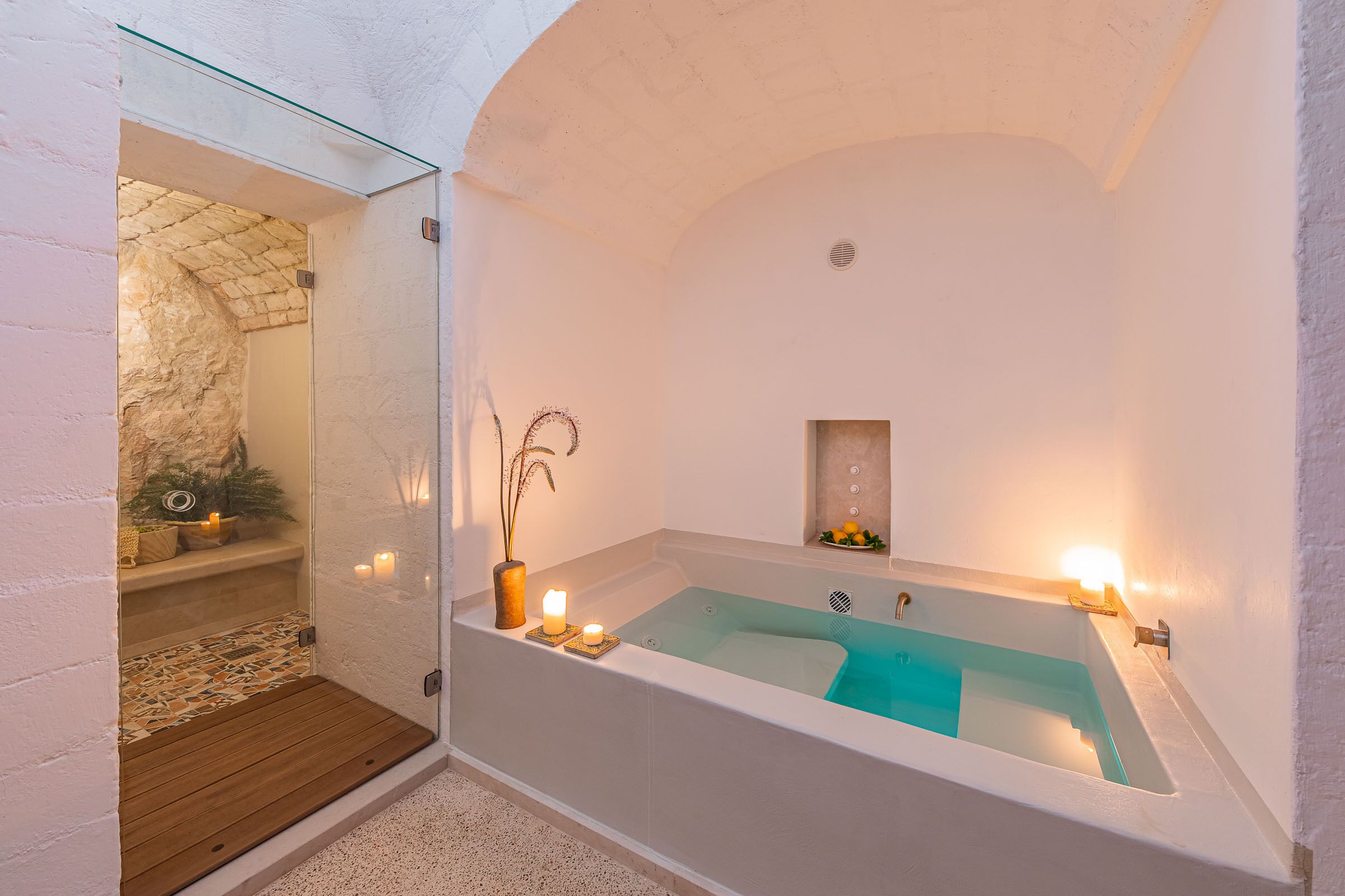 Un baño moderno con una bañera independiente, un estante pequeño con velas y una pared de piedra.