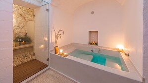 A modern bathroom with a freestanding bathtub, a small shelf with candles, and a stone wall.